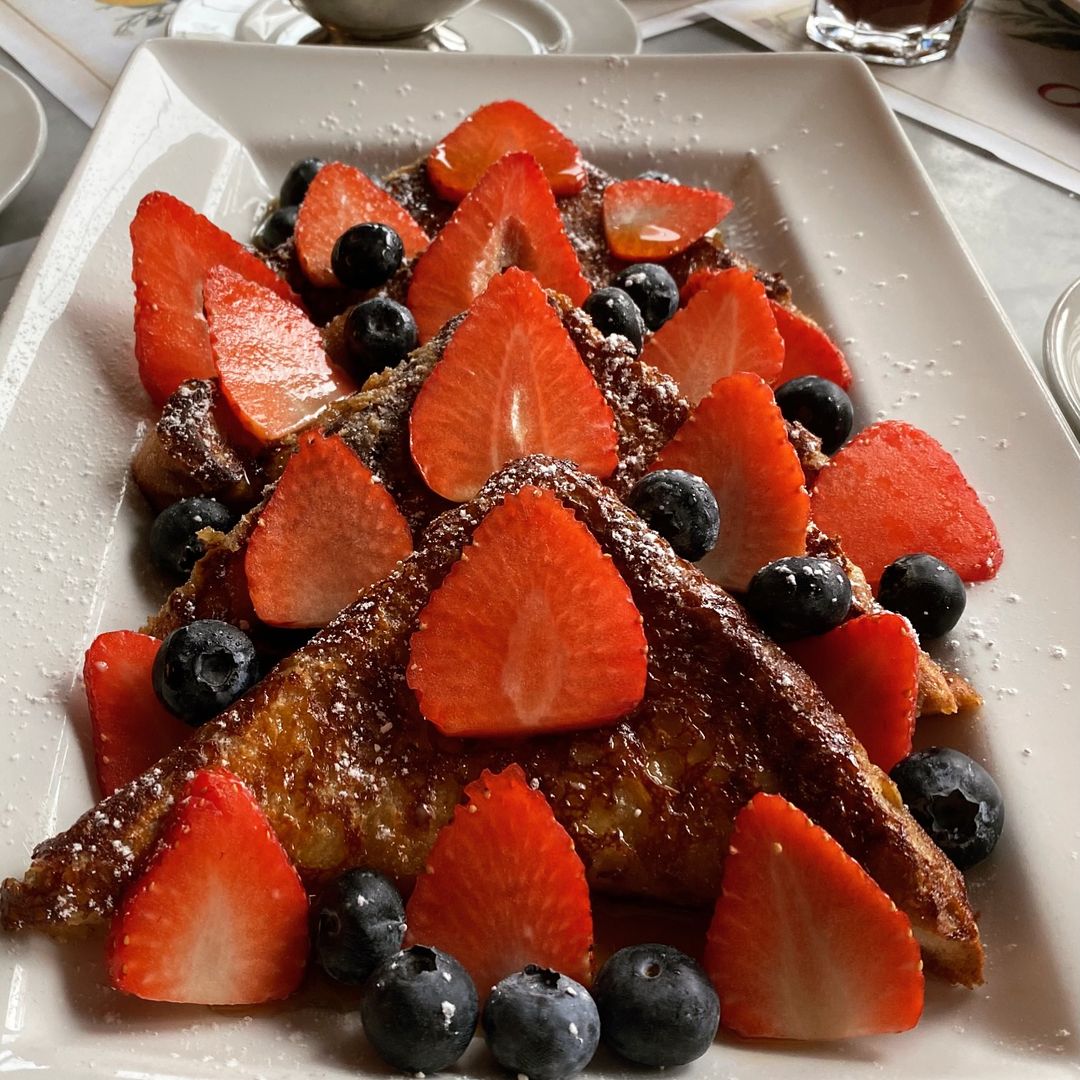 A healthy breakfast of French toast topped with fresh strawberries and blueberries on a white plate.