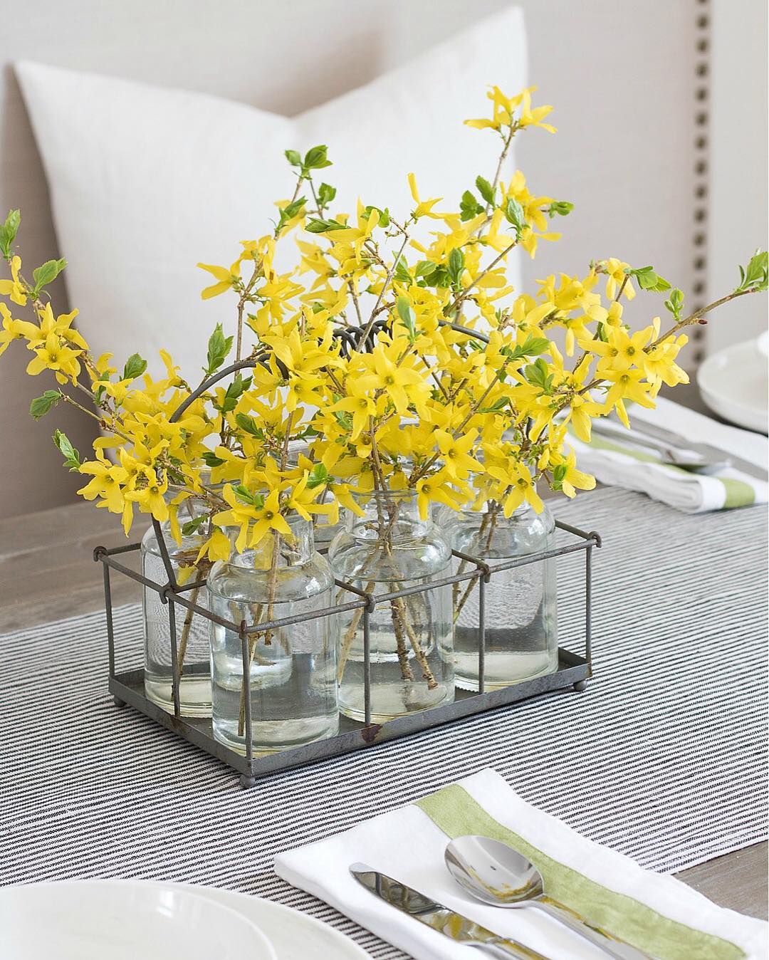A table adorned with glass vases filled with vibrant yellow forsythia flowers, creating a cheerful and bright atmosphere.