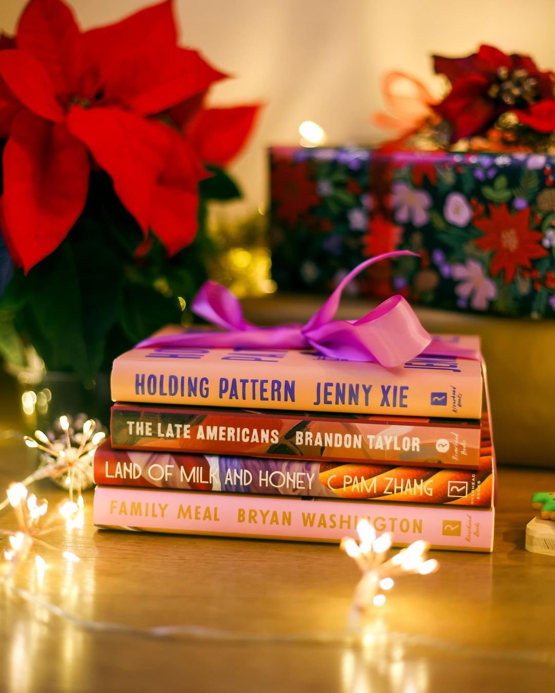 Books wrapped as a gift with a purple ribbon, displayed beside a Christmas tree.