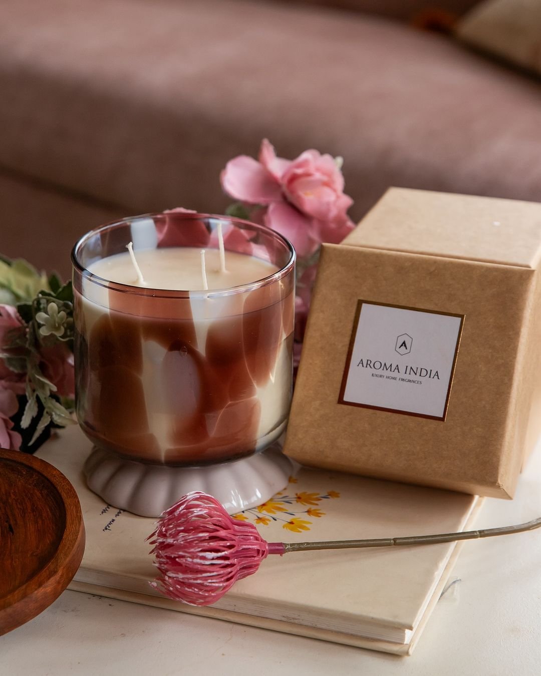 A scented candle next to a book and flowers on a table.