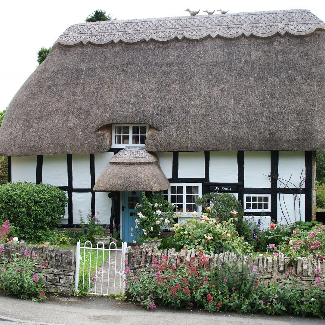  A picturesque thatched cottage with a white fence, adorned with colorful flowers, reminiscent of a fairy tale garden.
