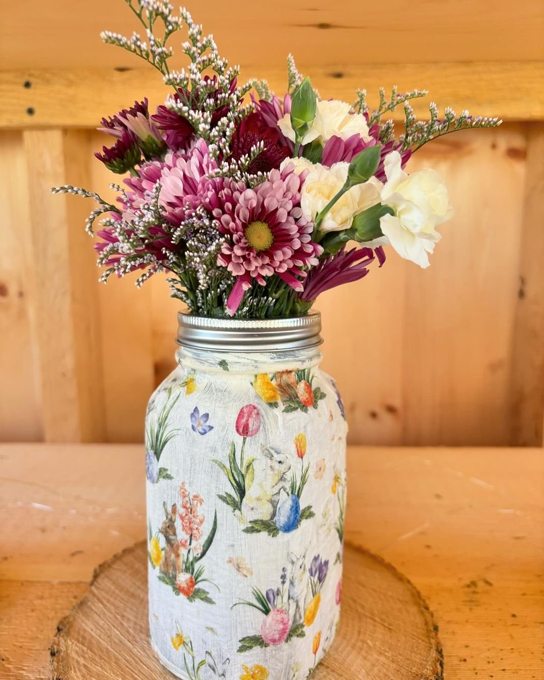 A mason jar filled with vibrant flowers sits elegantly on a rustic wooden table, adding charm to the setting.