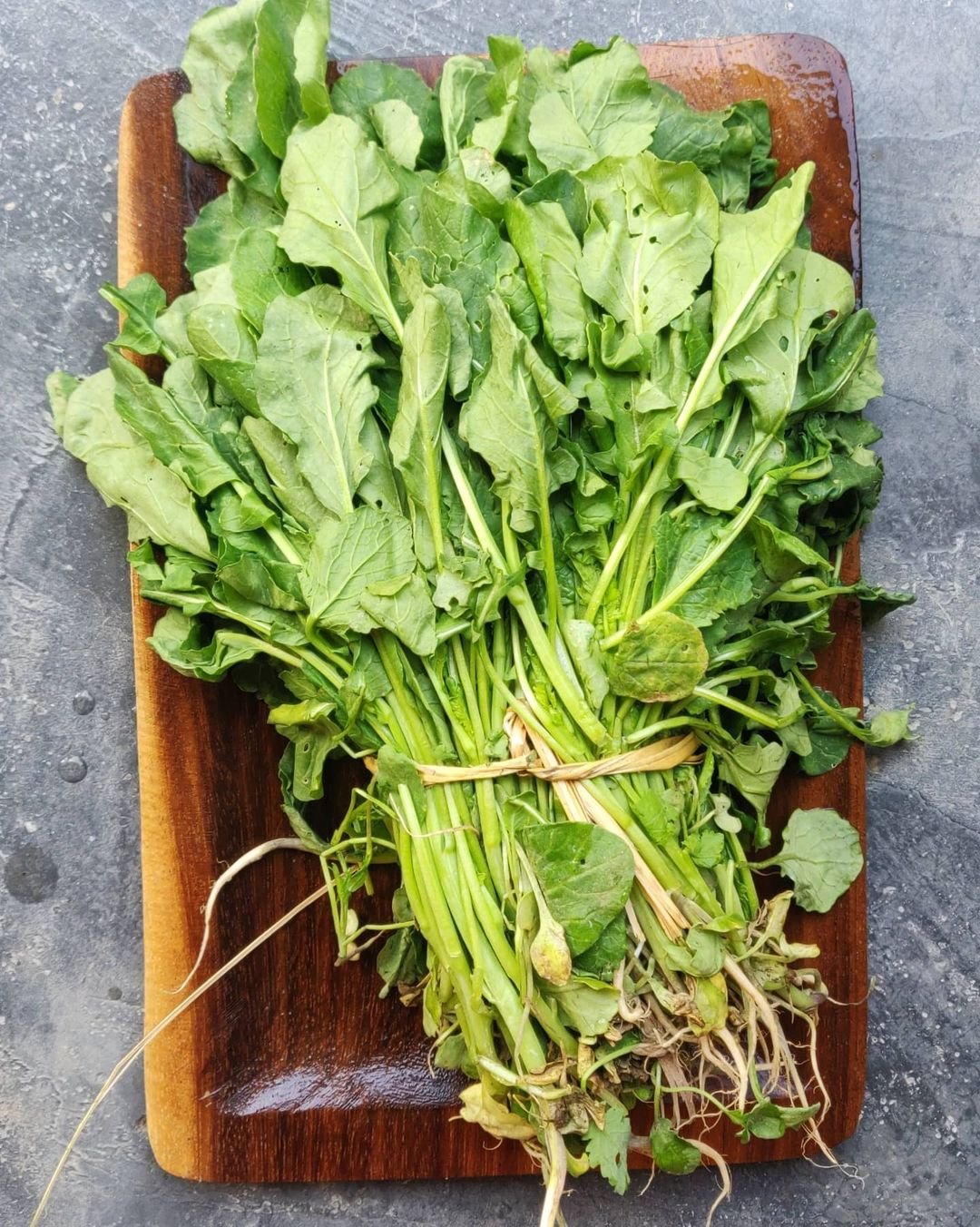 A basket of green vegetables, including Dwarf Bok Choy, on a wooden table.