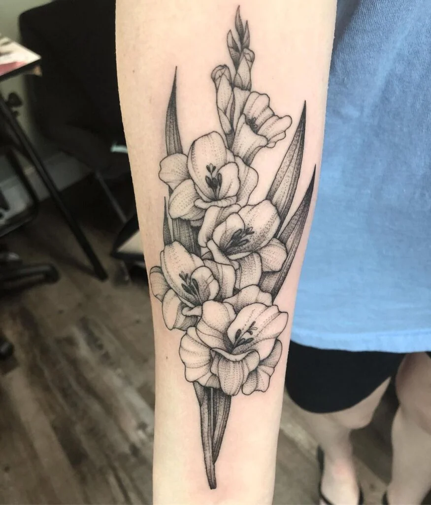 A gladiolus tattoo often symbolizes strength, honor, and remembrance, inspired by the flower's association with resilience and moral integrity.