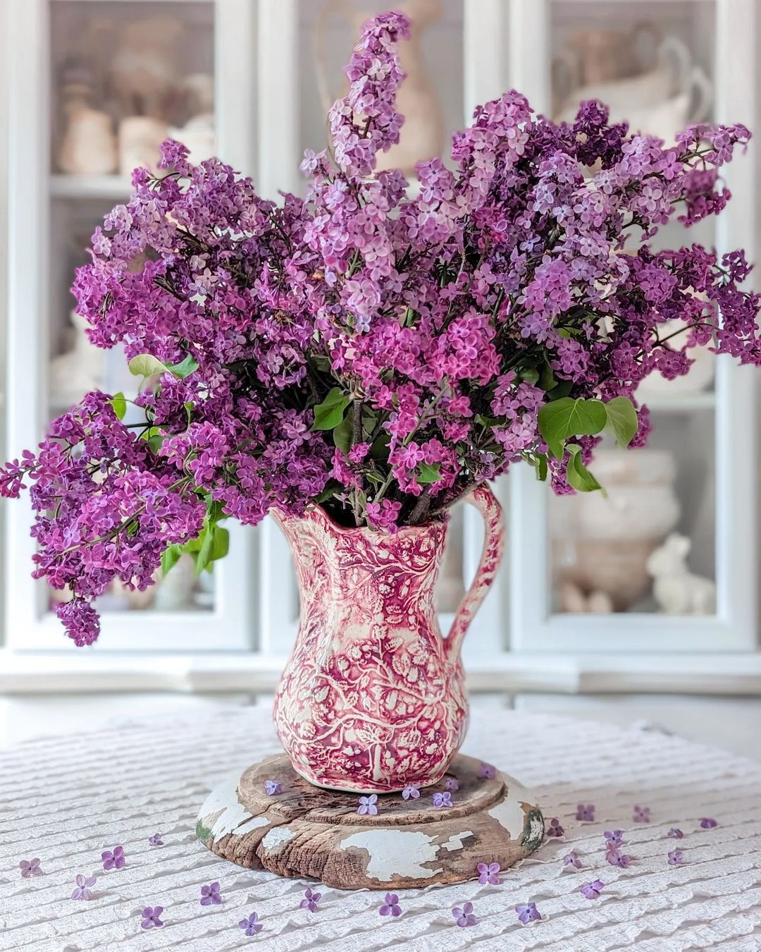 A vase filled with lilacs in shades of purple rests elegantly on a wooden table, adding a touch of beauty to the setting.