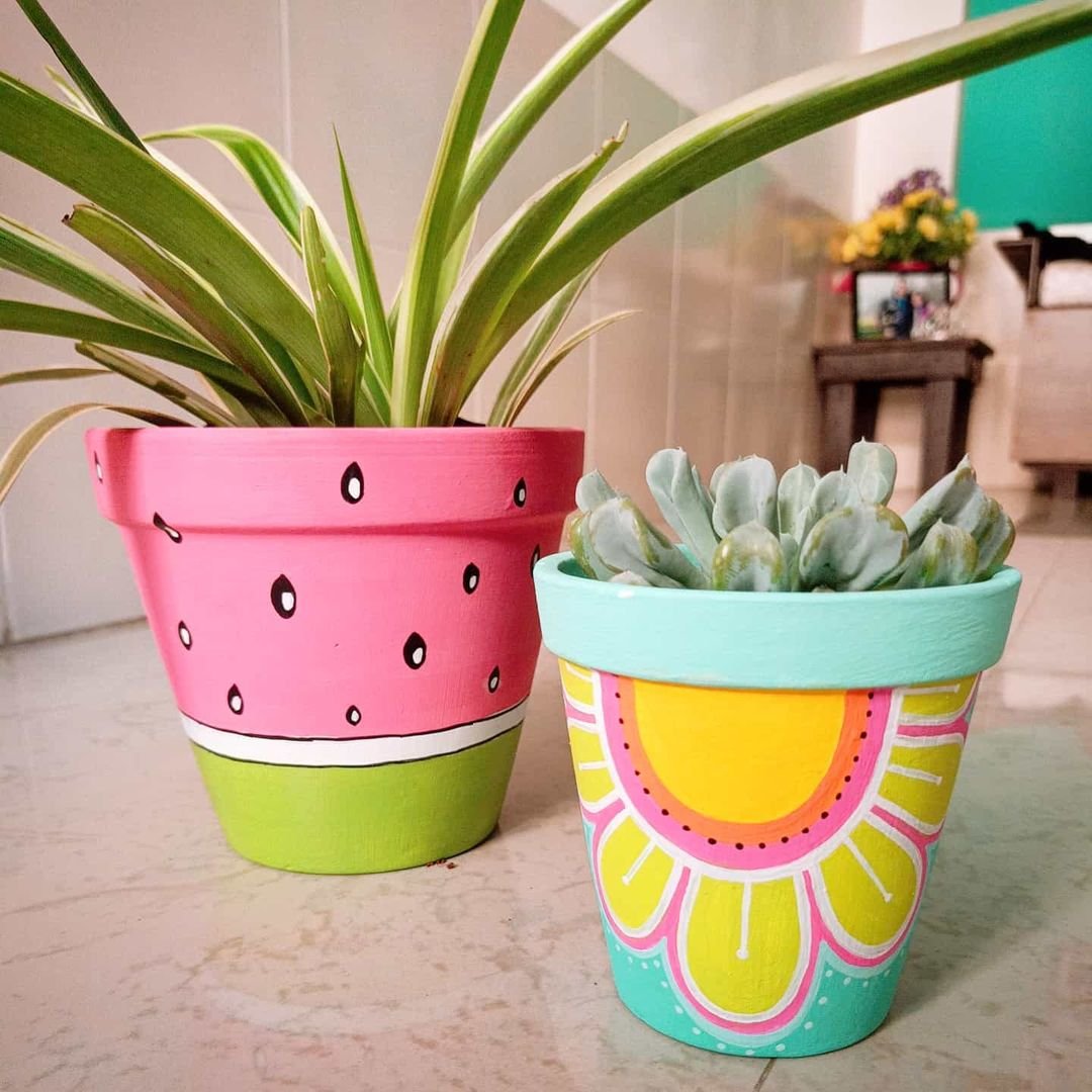 Two terracotta flower pots featuring vibrant watermelon and sunflower designs, each containing lush succulents.
