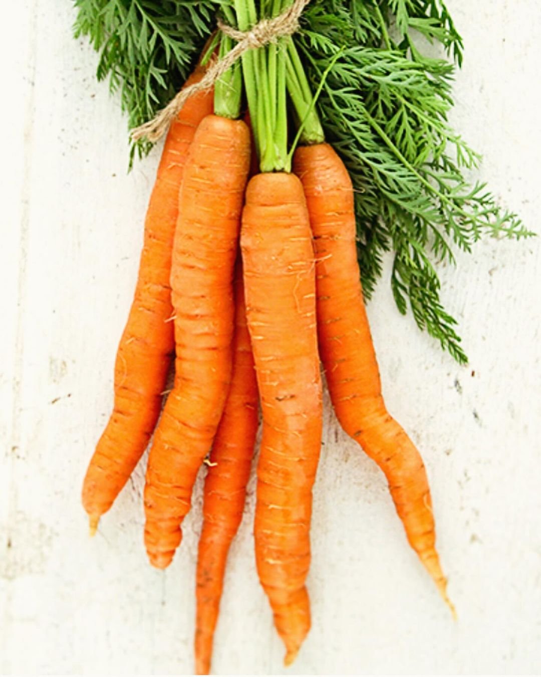 A bunch of fresh carrots suspended from a rope, showcasing their vibrant orange color and green tops.