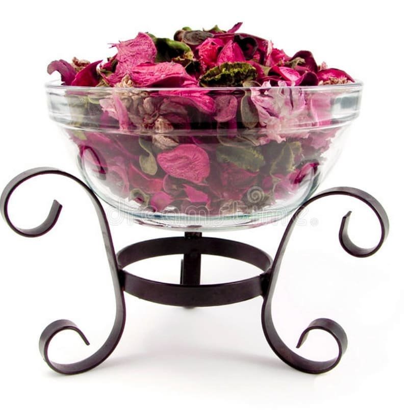  A glass bowl filled with dried rose petals, elegantly displayed on a stand, showcasing a beautiful potpourri arrangement.