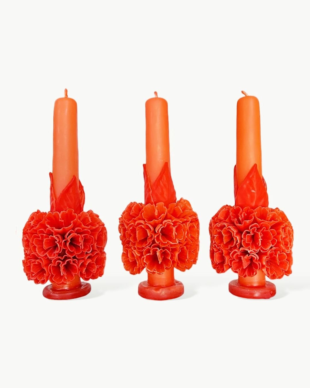 Three orange floral beeswax candles adorned with vibrant flowers, creating a warm and inviting atmosphere.